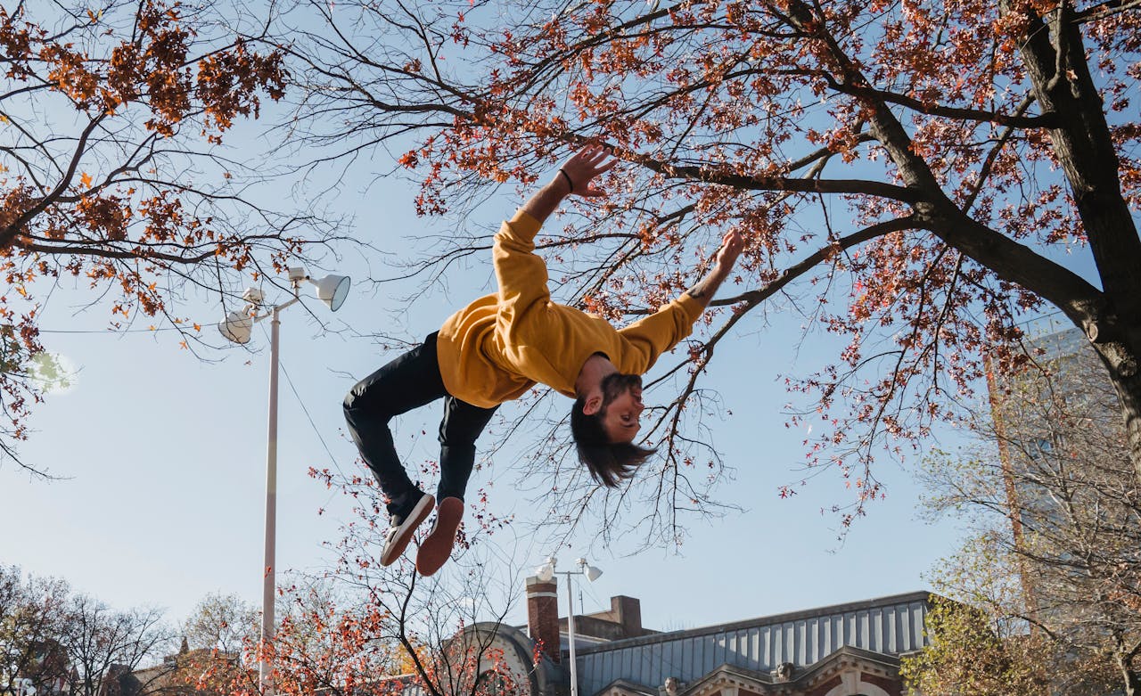 Dynamic action shot of a young man performing a backflip in an urban park setting during fall.